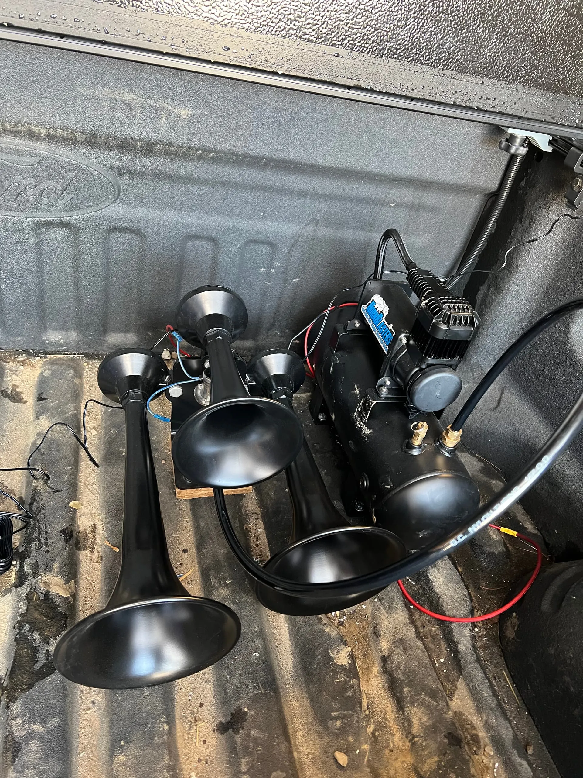 Three black train horn trumpets and air compressor system installed in the bed of Jimmy's Ford F250