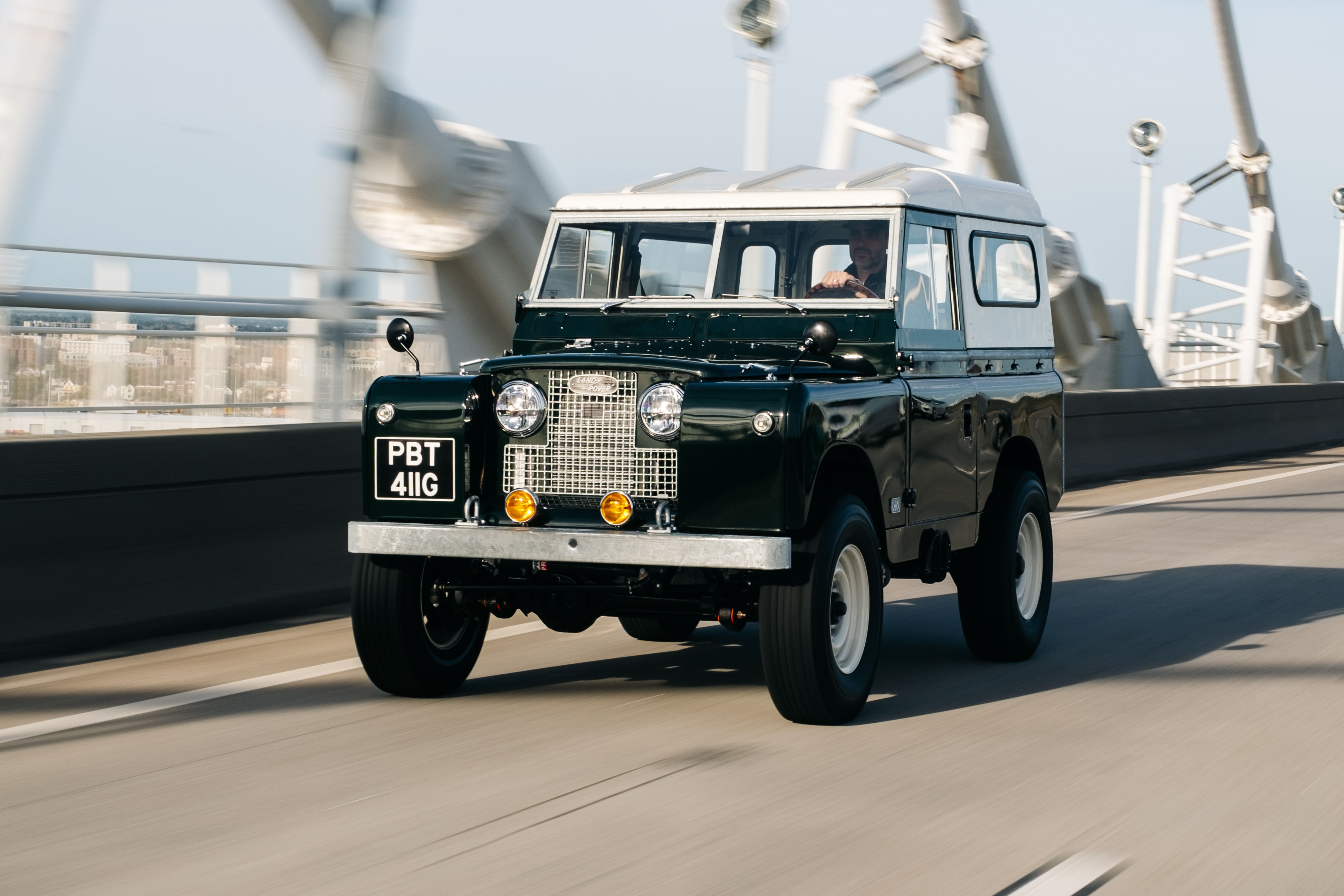 A classic green Land Rover driving on a bridge.