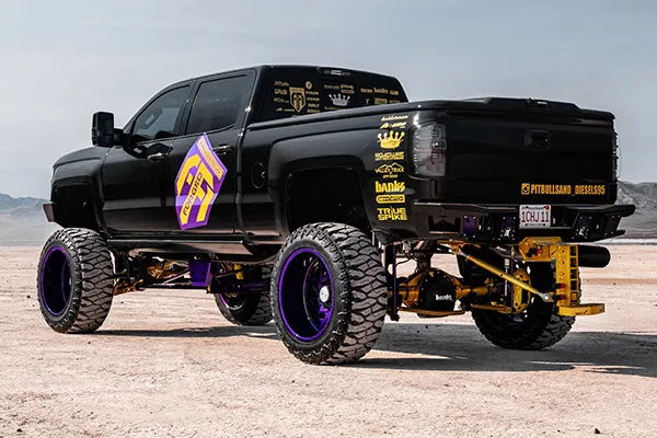 Rear three-quarter view of Nicholas's black lifted 2016 Chevy Silverado 2500HD with purple wheels and custom suspension, install photo 3