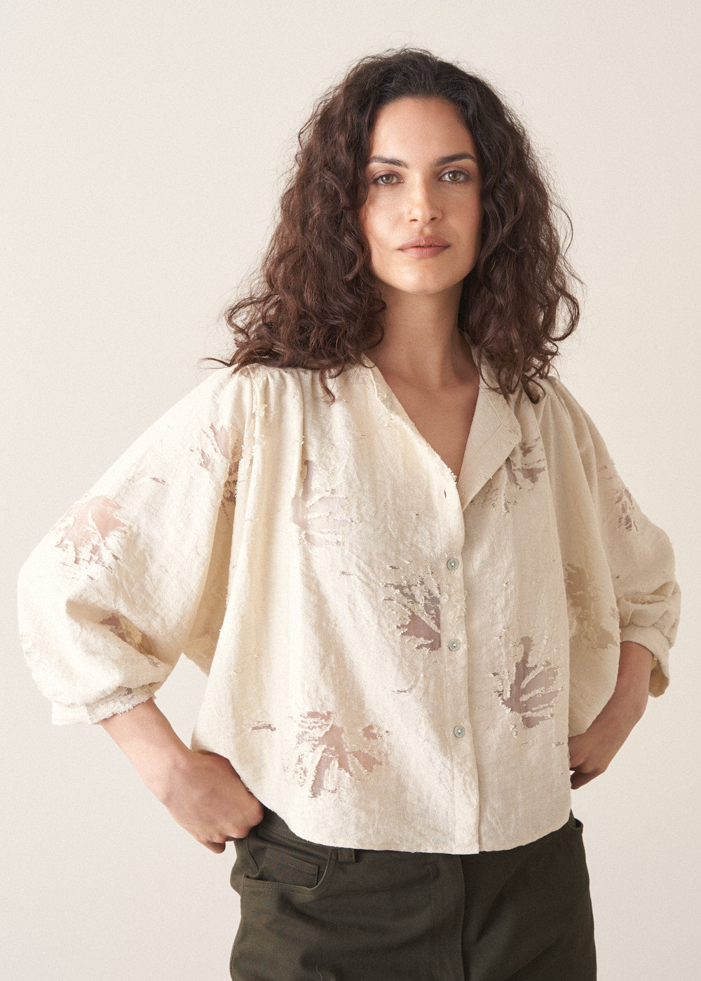 Woman wearing light cream devoree jacquard textured shirt and green trousers