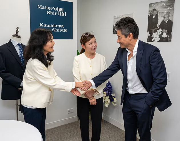 Two people shaking hands, with another person observing in a professional setting.