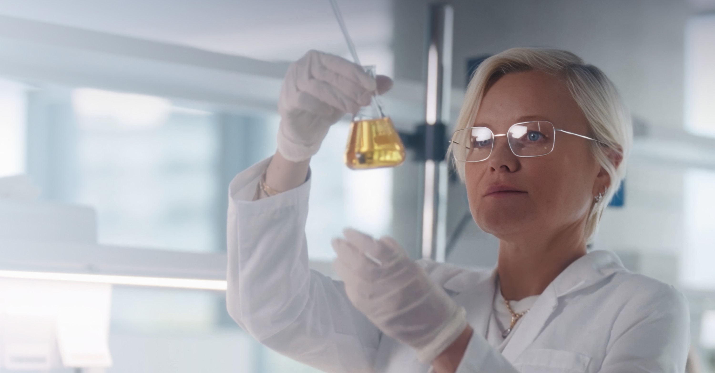 Scientist in lab coat holding a beaker, examining a liquid.