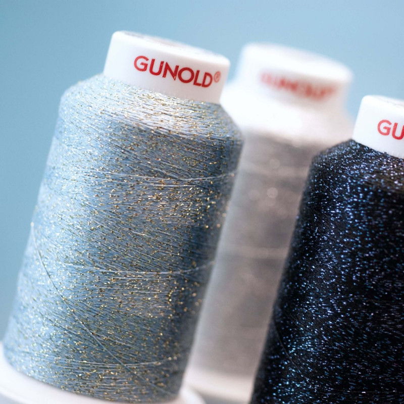 Metallic embroidery thread cones in blue, silver and black with reflective sparkle fibres in the thread, on textured spools