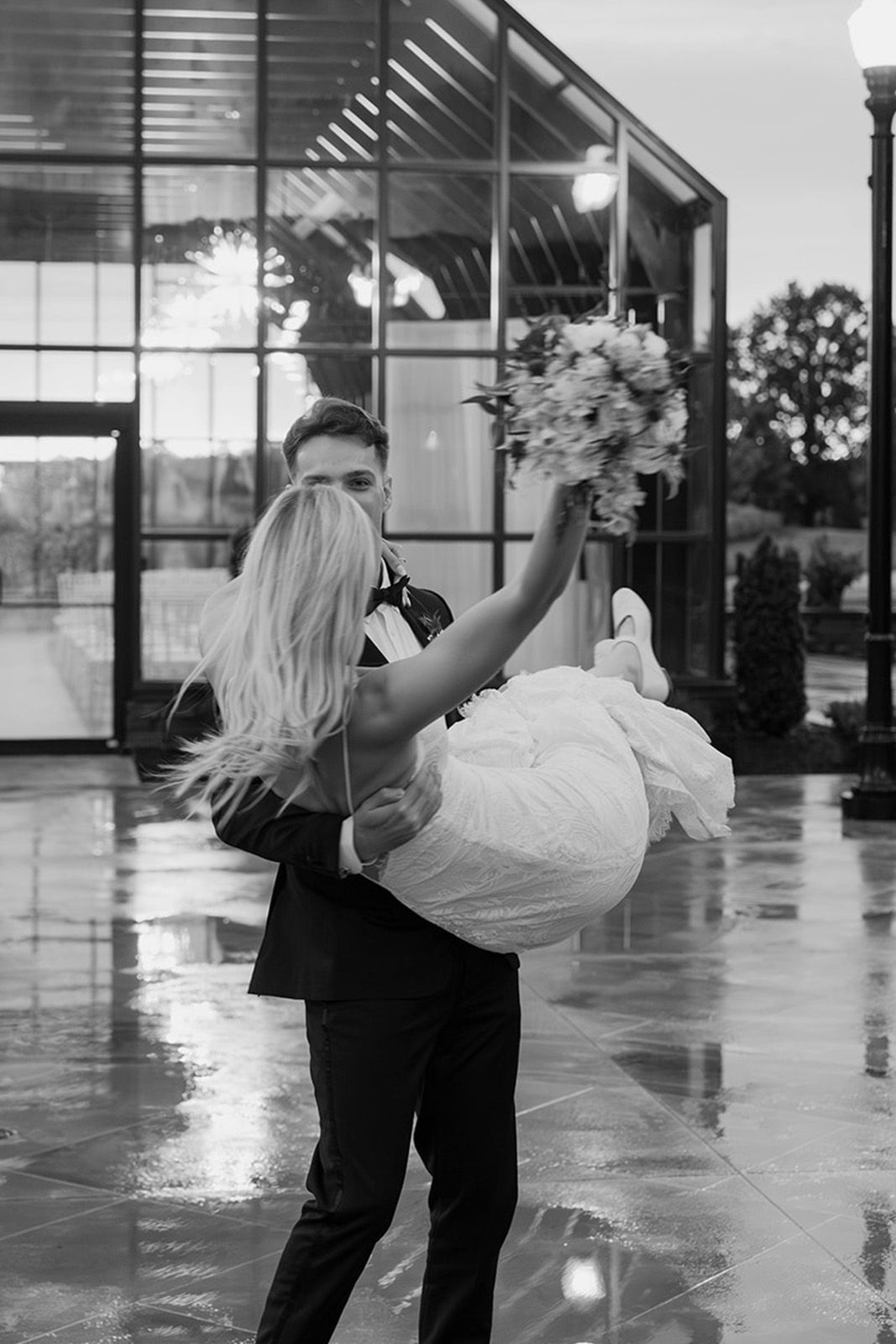 Couple in wedding attire, groom lifting bride outdoors with flowers.