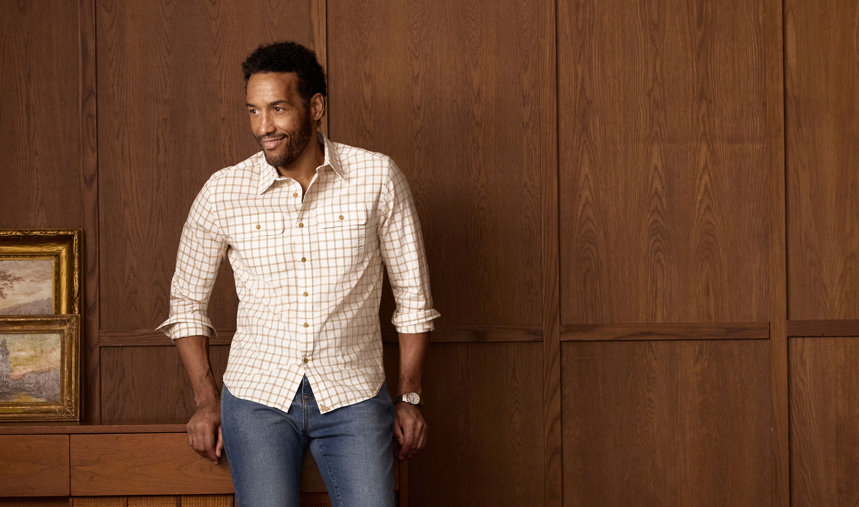 Man standing in a room with wooden walls, wearing a light shirt and jeans.