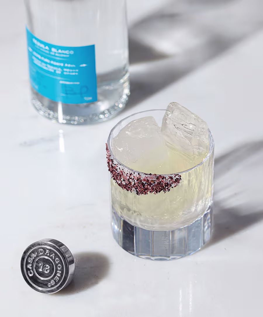 A cocktail glass with ice and a bottle in the background.