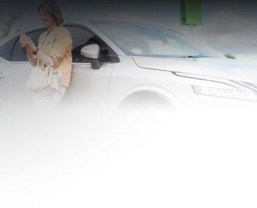 A person standing next to a white car, looking at their phone.