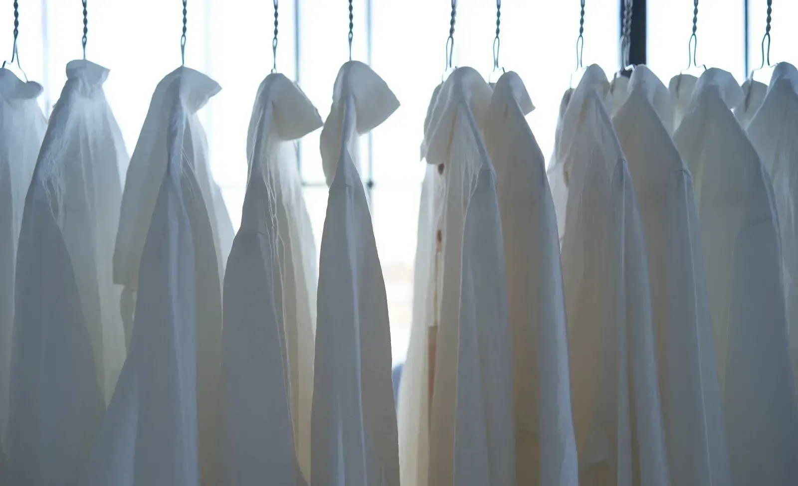 A set of white undyed shirts sit on a clothing rack.