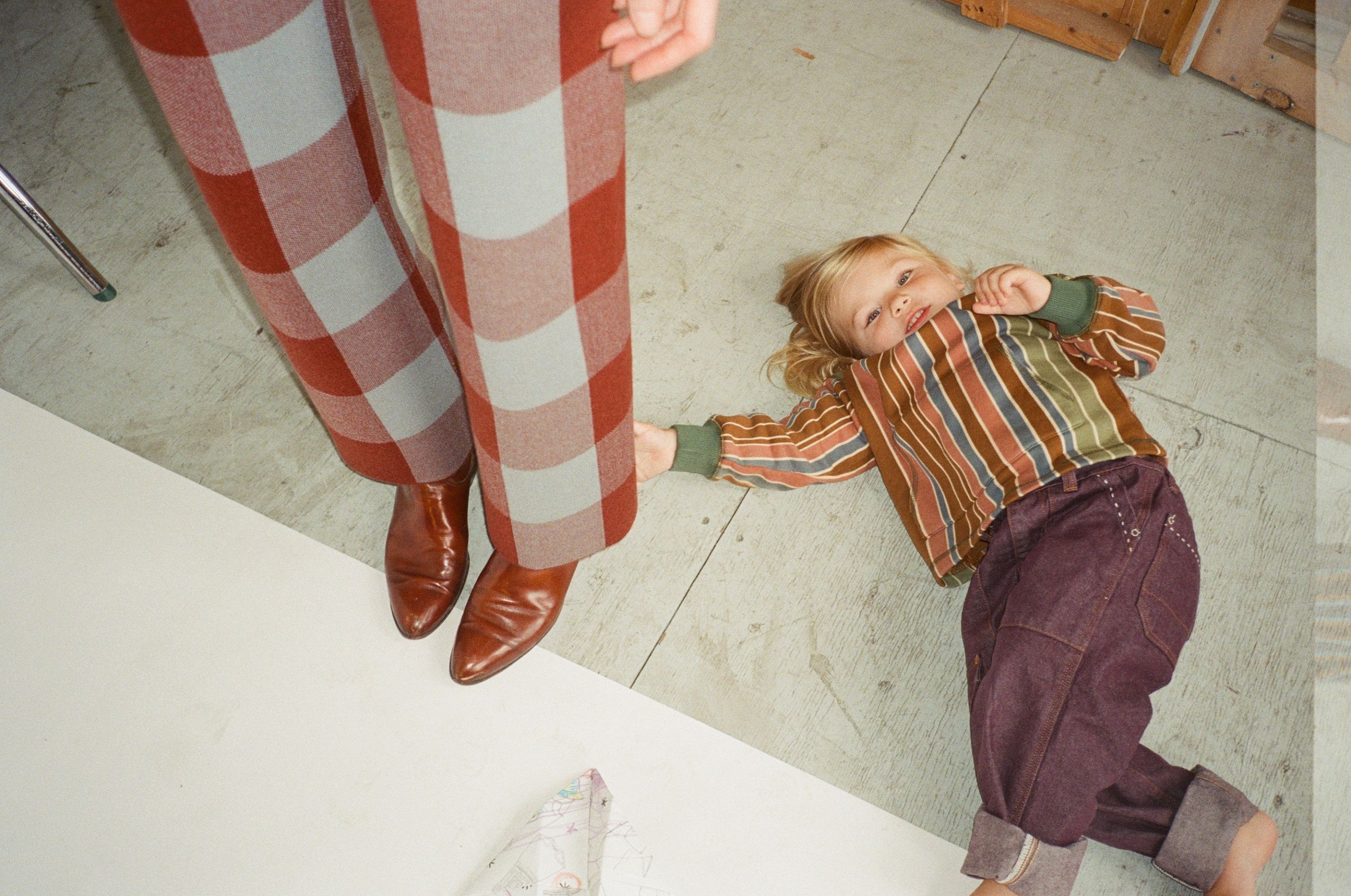A child lying on the floor next to an adult's feet.