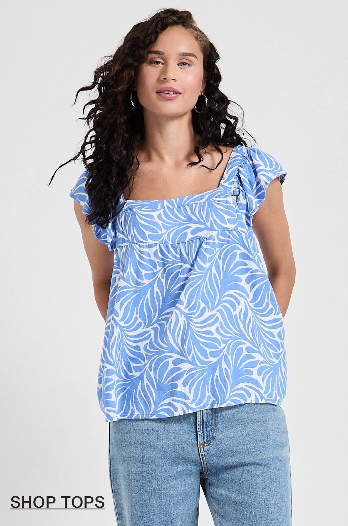 Woman wearing a blue patterned top with ruffled sleeves and jeans.