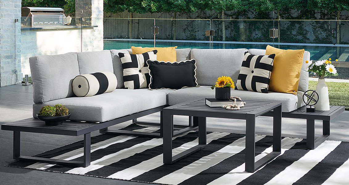 Outdoor sectional sofa with pillows on a striped rug by a pool.