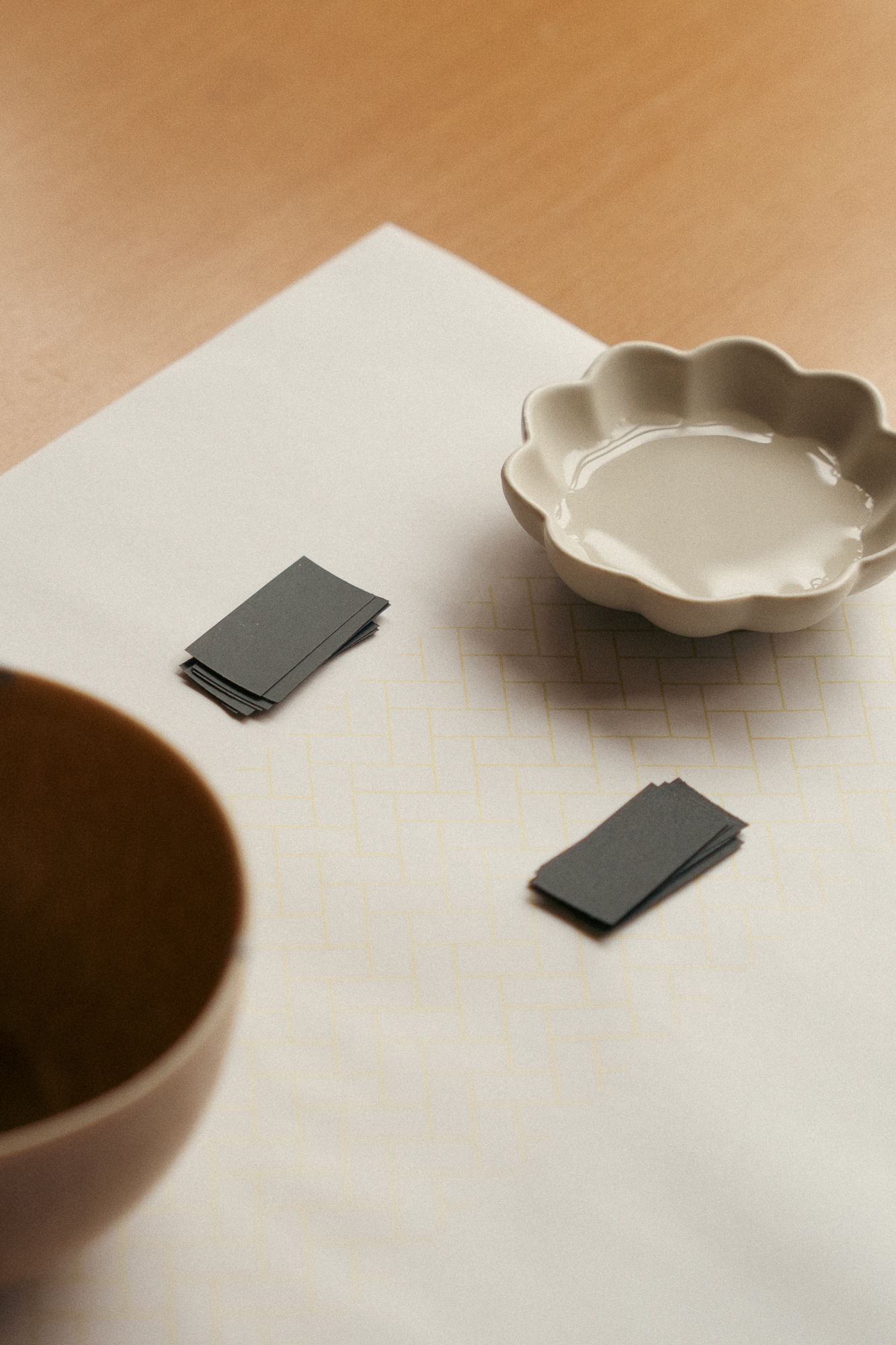 Bowl, dish, and two rectangular objects on a tablecloth.
