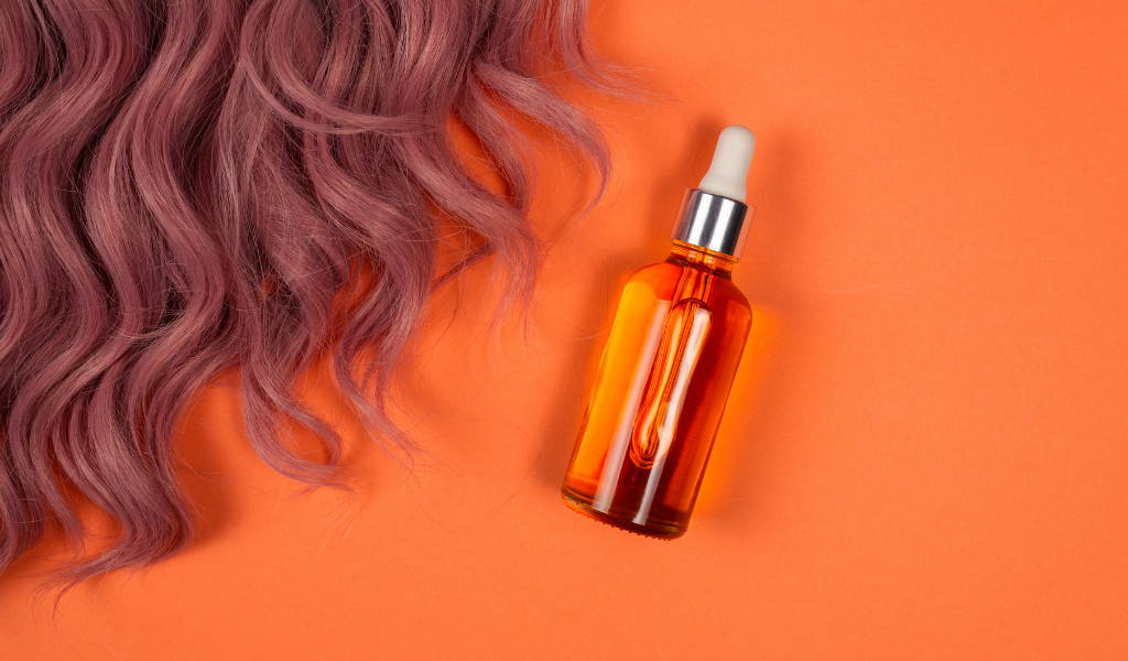 A bottle of essential oils on orange background next to woman's hair