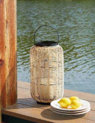 A wicker lantern sits on a wooden ledge in front of a lake, A plate of lemon sits beside the latern.