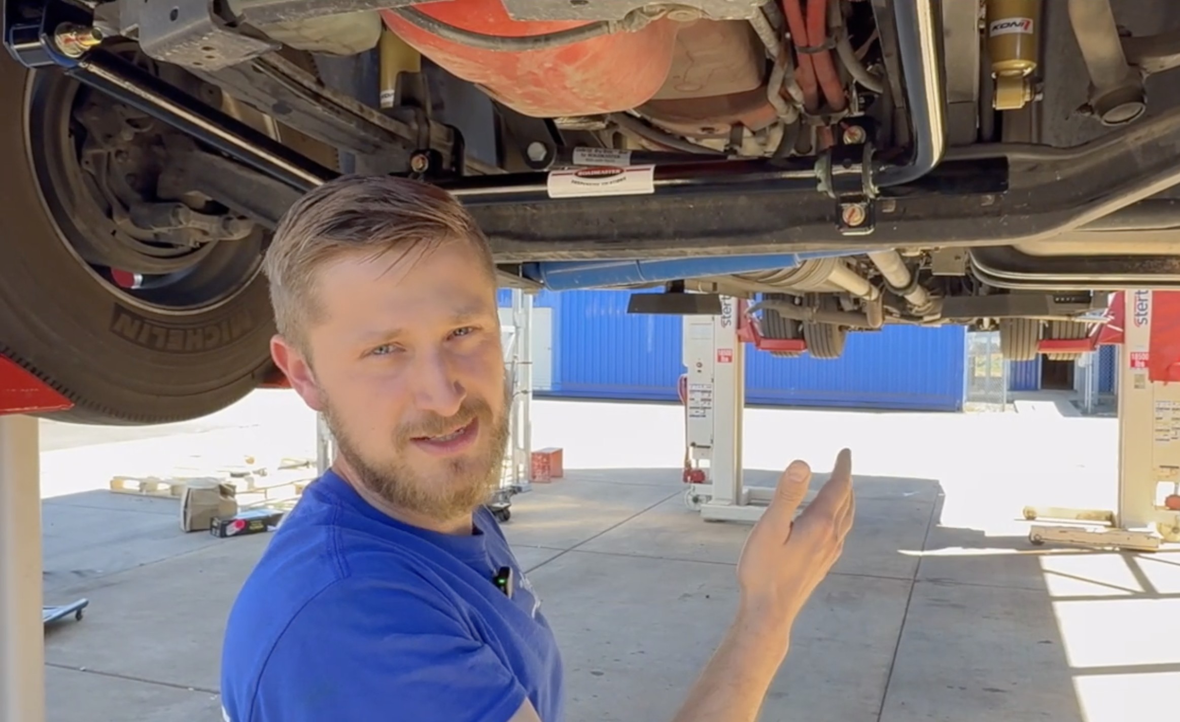 Mechanic working under a vehicle, pointing and explaining a component.