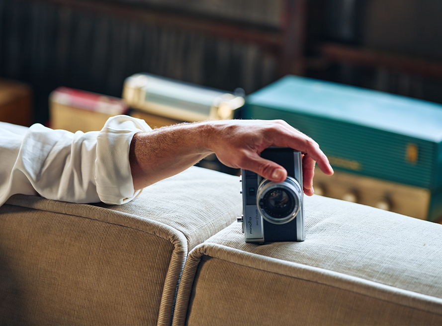 A hand resting on a camera placed on a sofa.