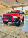 Lifted red Ram 1500 with LED light bars and train horns visible through grille in car wash bay