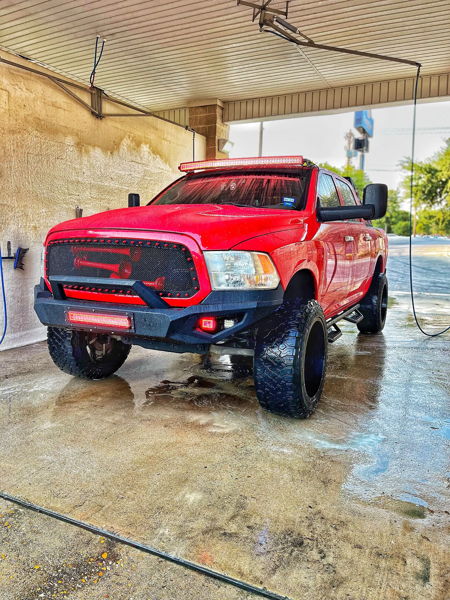 Lifted red Ram 1500 with LED light bars and train horns visible through grille in car wash bay