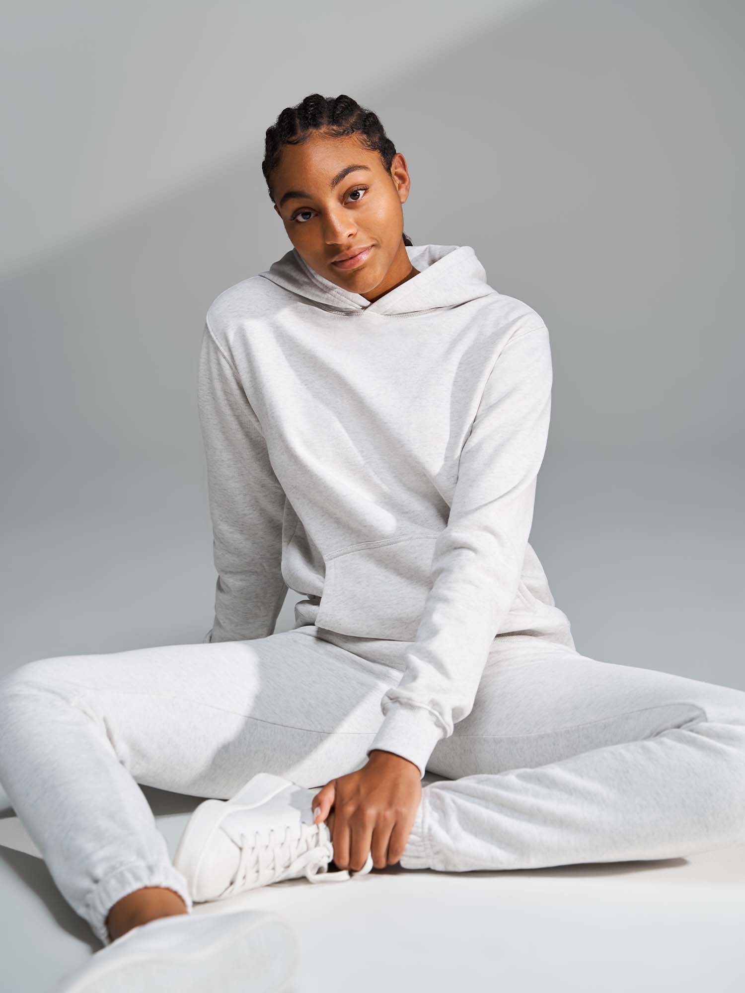 Tall woman wearing a heather cloud white hoodie and sweatpants sitting on the ground