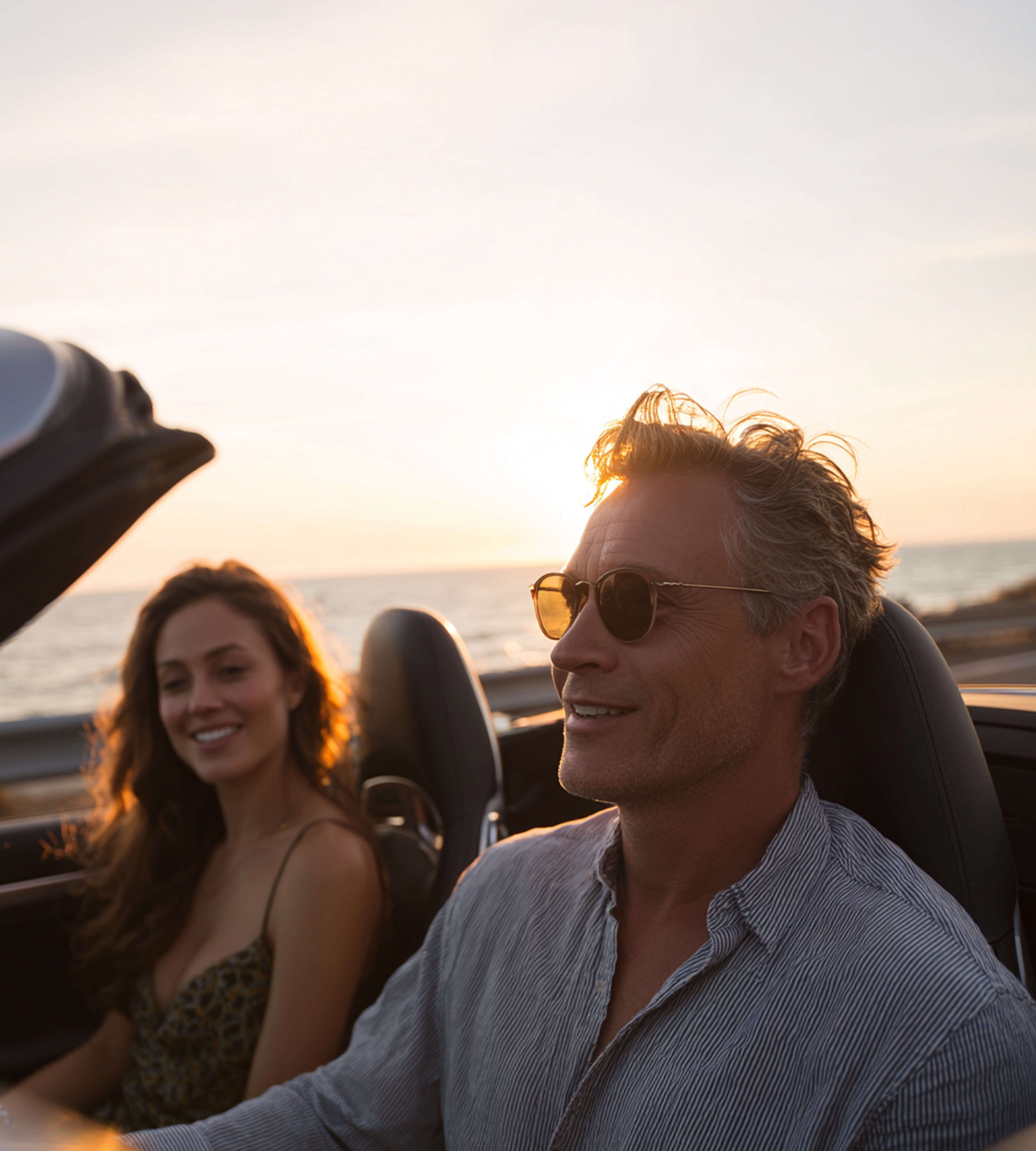 Una pareja disfrutando de un paseo al atardecer en un coche descapotable.