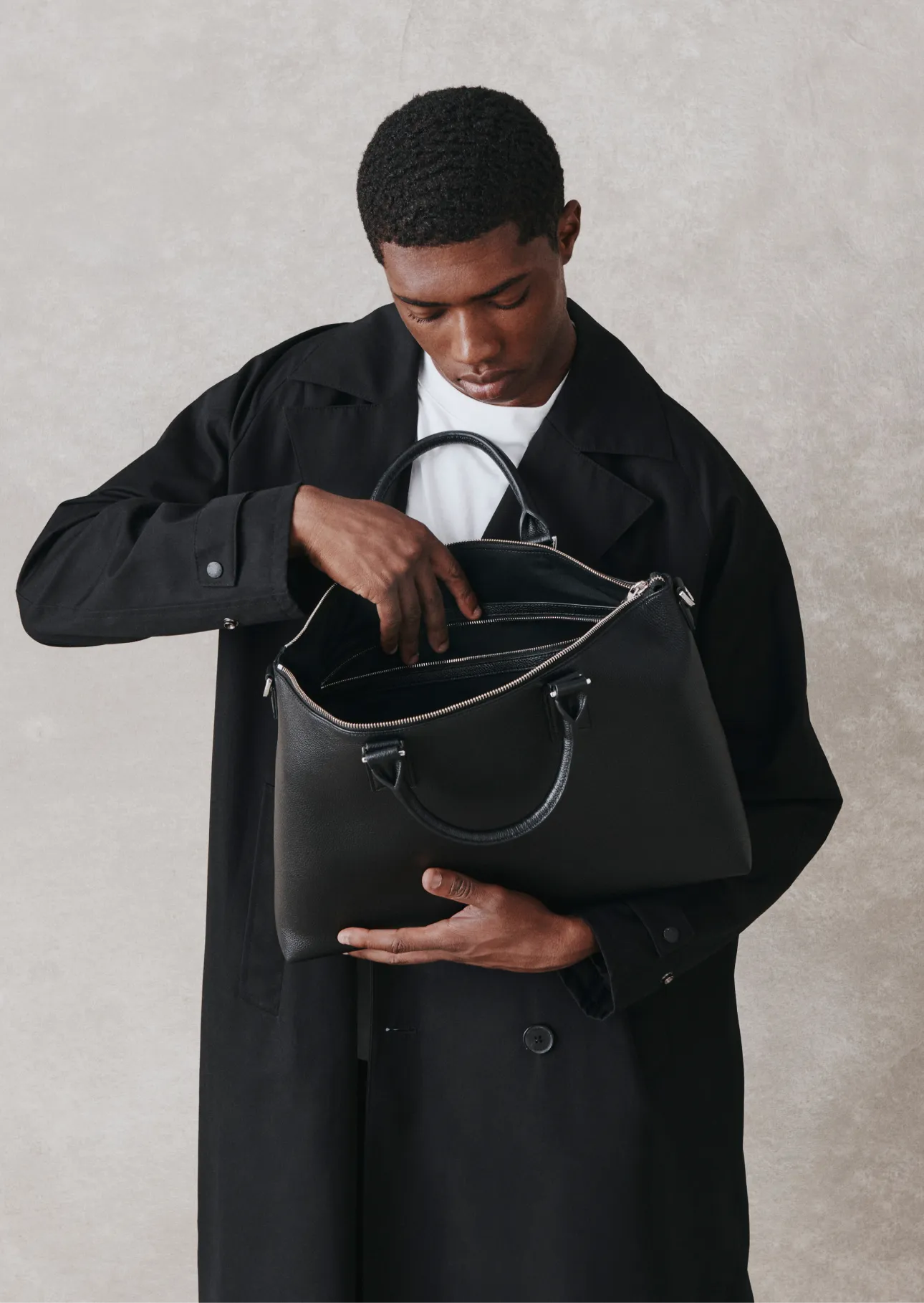 A man in a black coat examines a black handbag.