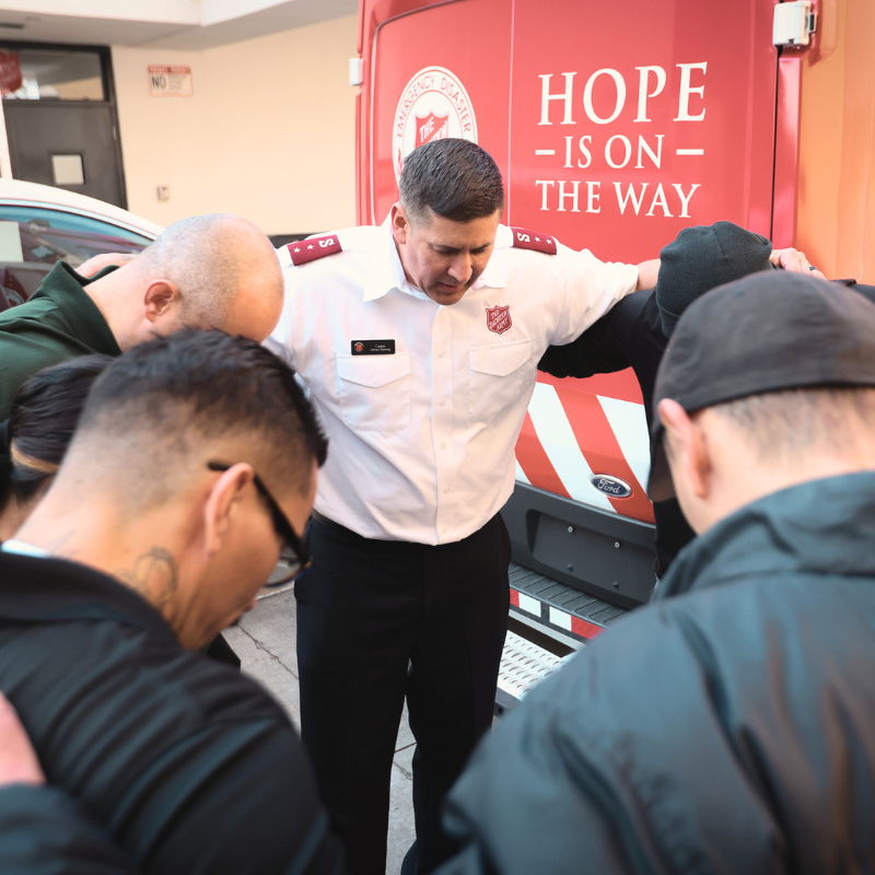 People praying together near a Salvation Army vehicle.