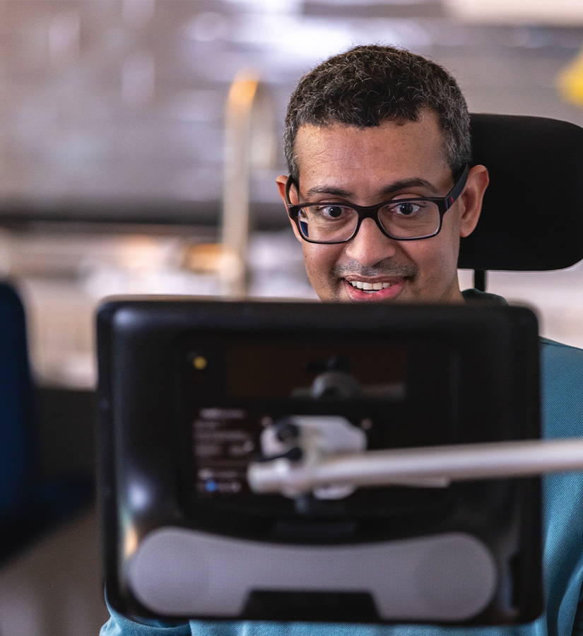 一位坐在轮椅前微笑的男士，面前是一台沟通设备。