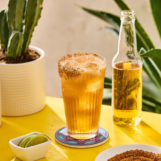 A refreshing drink with lime and a bottle on a yellow table.