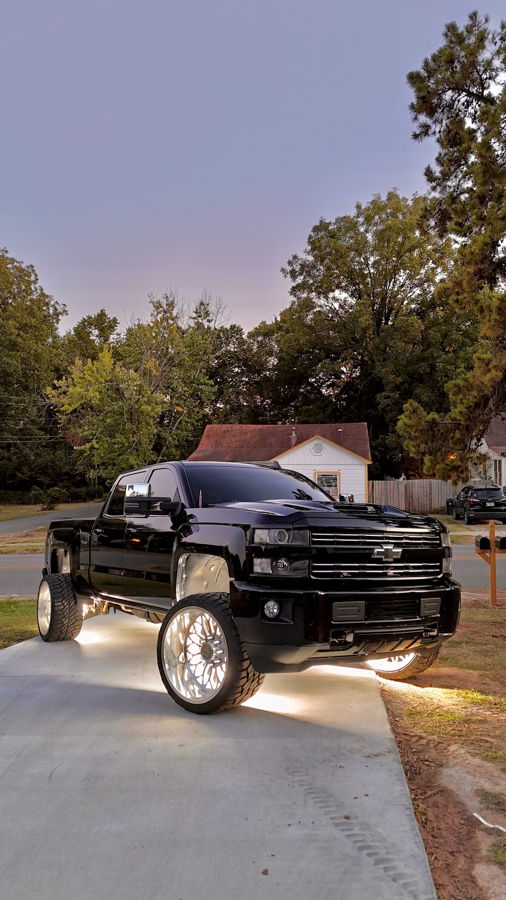 Front-three-quarter Craig's lifted black 2016 Chevrolet Silverado 2500HD crew cab heavy-duty pickup HornBlasters Conductor's Special 2HB Spare Tire Delete train horn kit customer install LED rock lights polished chrome wheels residential driveway dusk gallery photo 1