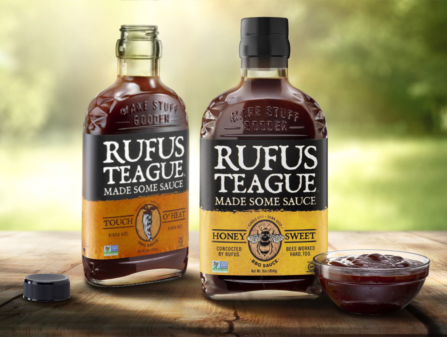 Two bottles of Rufus Teague barbecue sauce on a wooden surface.