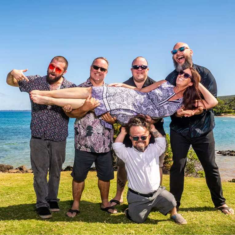Group of five people posing at the beach, one held up by others.