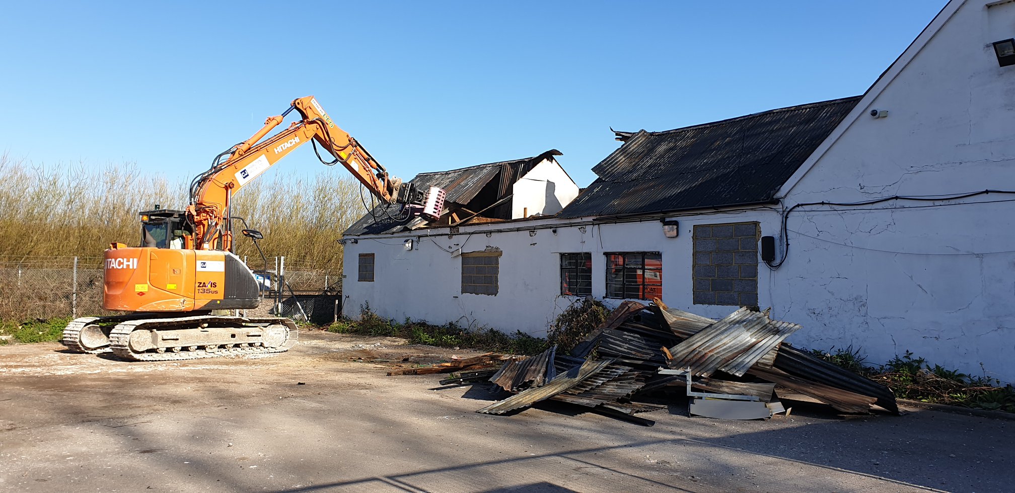 Excavator demolishing a building with debris scattered on the ground.