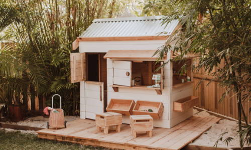 A pitched roof cubby house with wooden stools for residentials, signature cubby houses