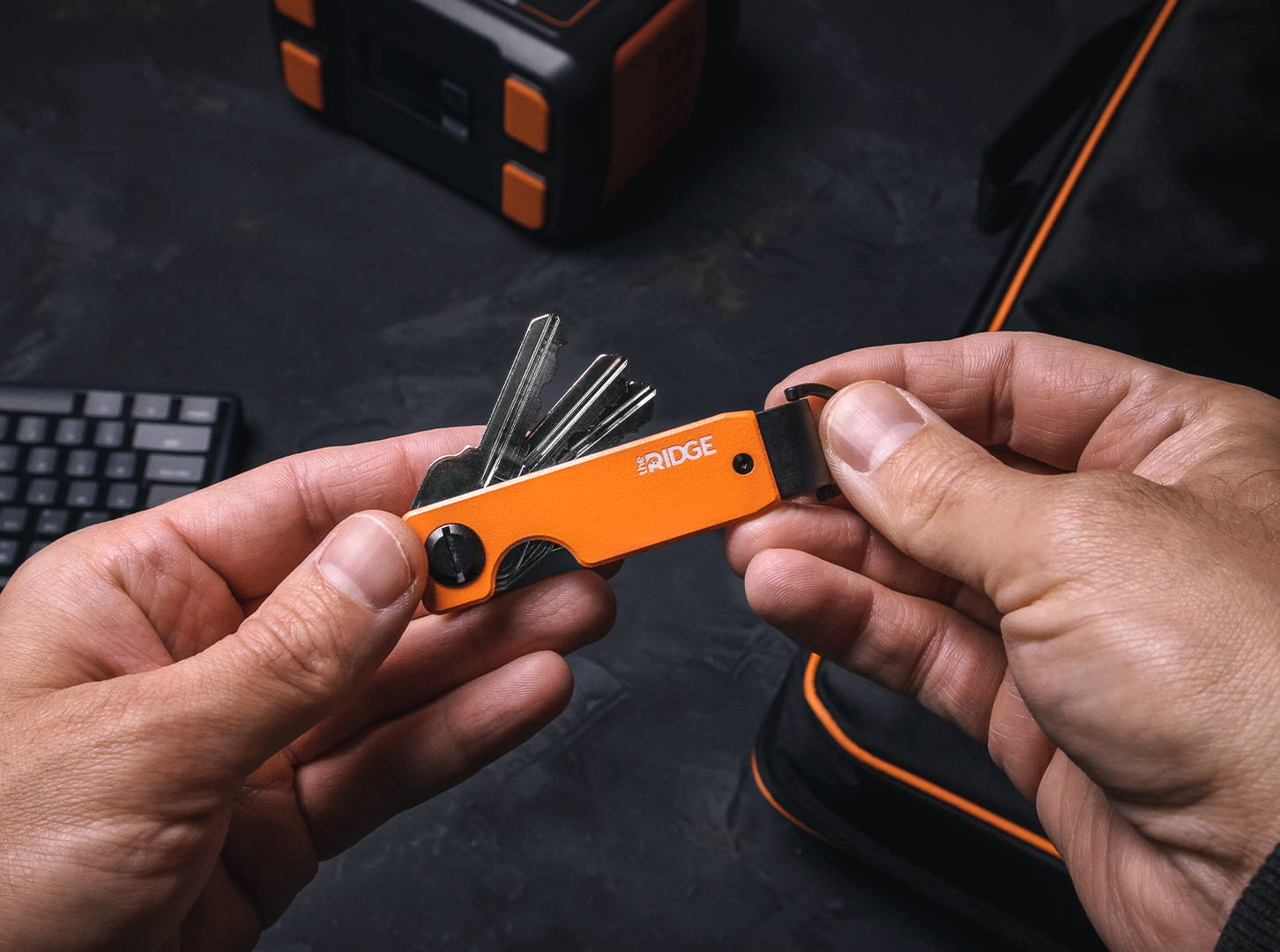 man holding a Ridge Basecamp Orange keycase with two hands