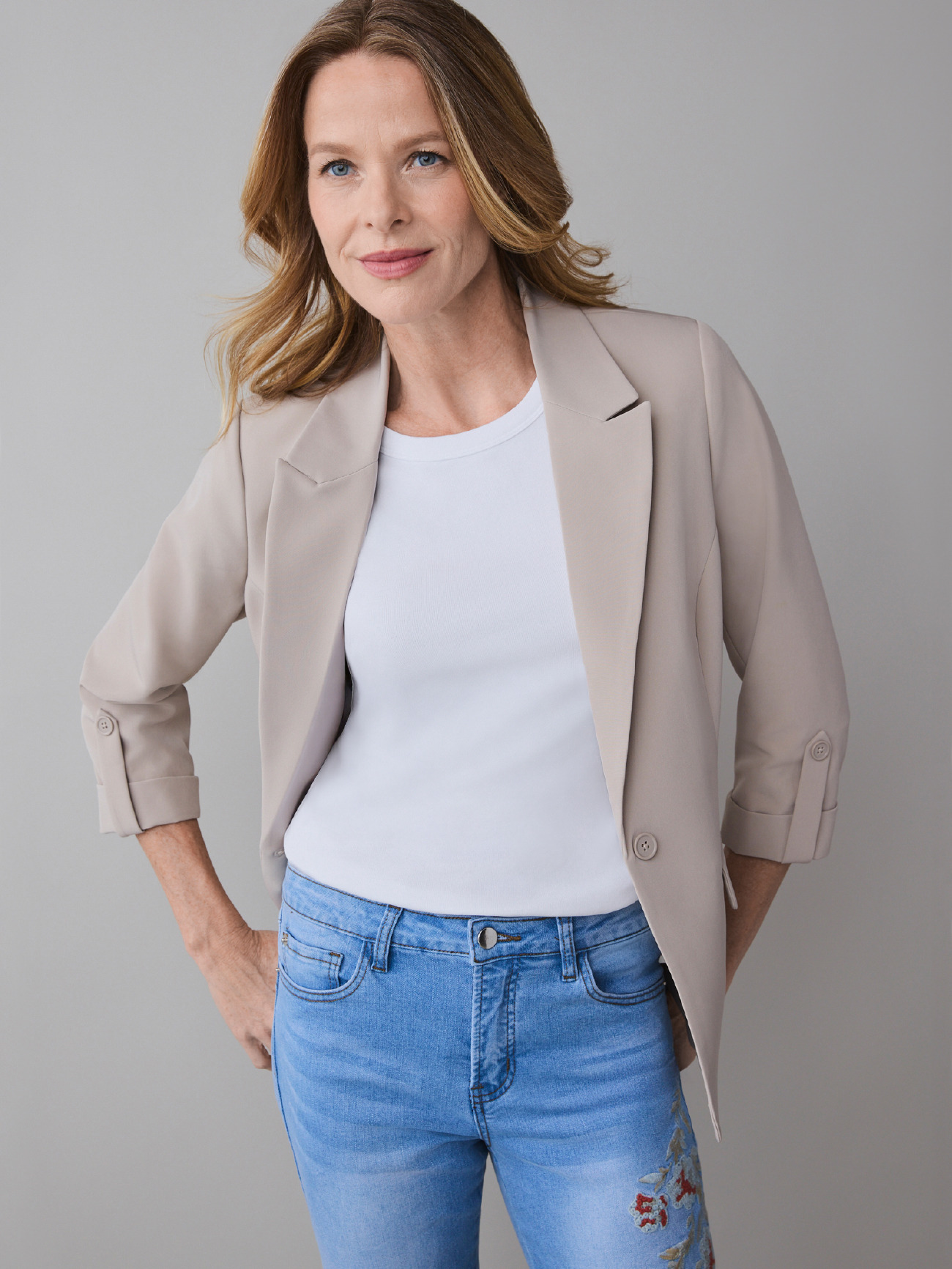 A woman in a beige blazer and white shirt poses confidently.