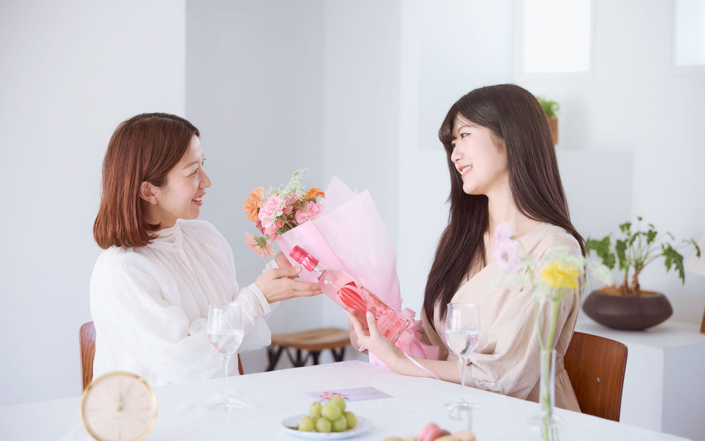 Two women exchanging a bouquet of flowers in a bright indoor setting.