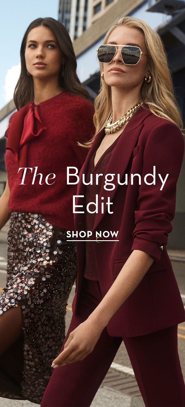 Two women model burgundy outfits in a stylish urban setting.