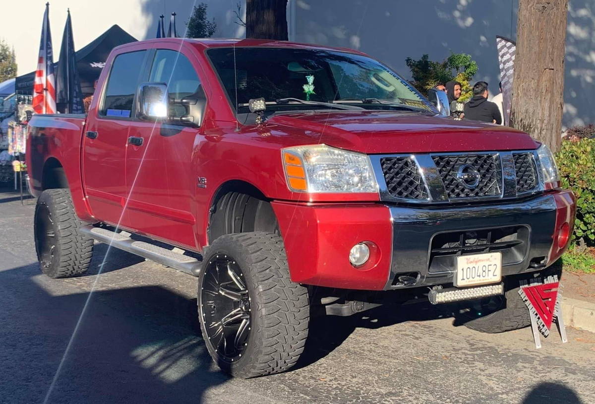 Front three-quarter view of Alexander's metallic red 2004 Nissan Titan LE V8 with lifted suspension and aftermarket wheels with HornBlasters Conductor's Special 244K Spare Tire Delete kit with S6 upgrade featured customer install gallery photo 1