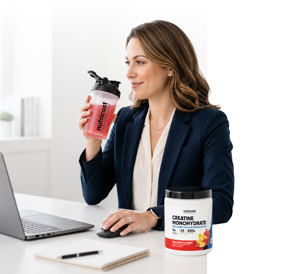 Woman in business attire drinking from a shaker while using a laptop.