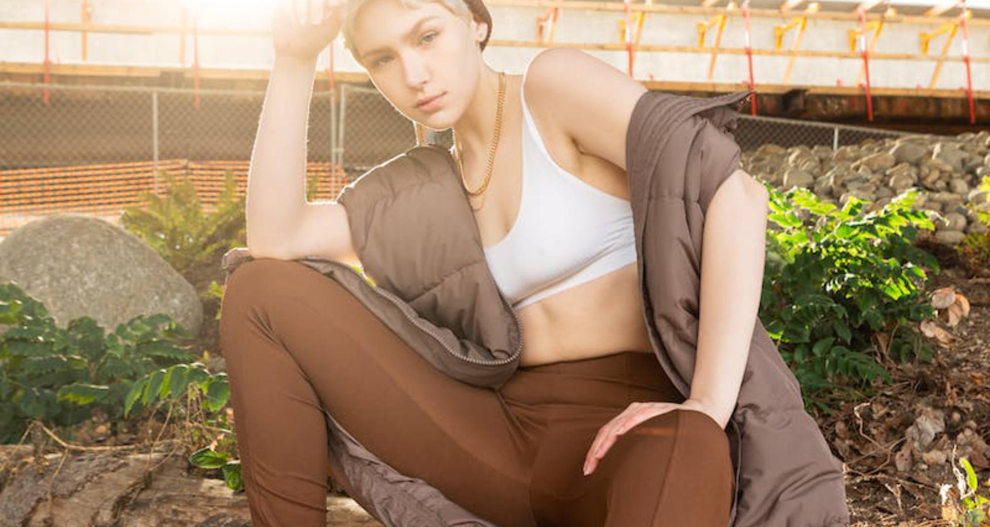 woman wearing a white bralette, brown track pants, and a brown puffy vest
