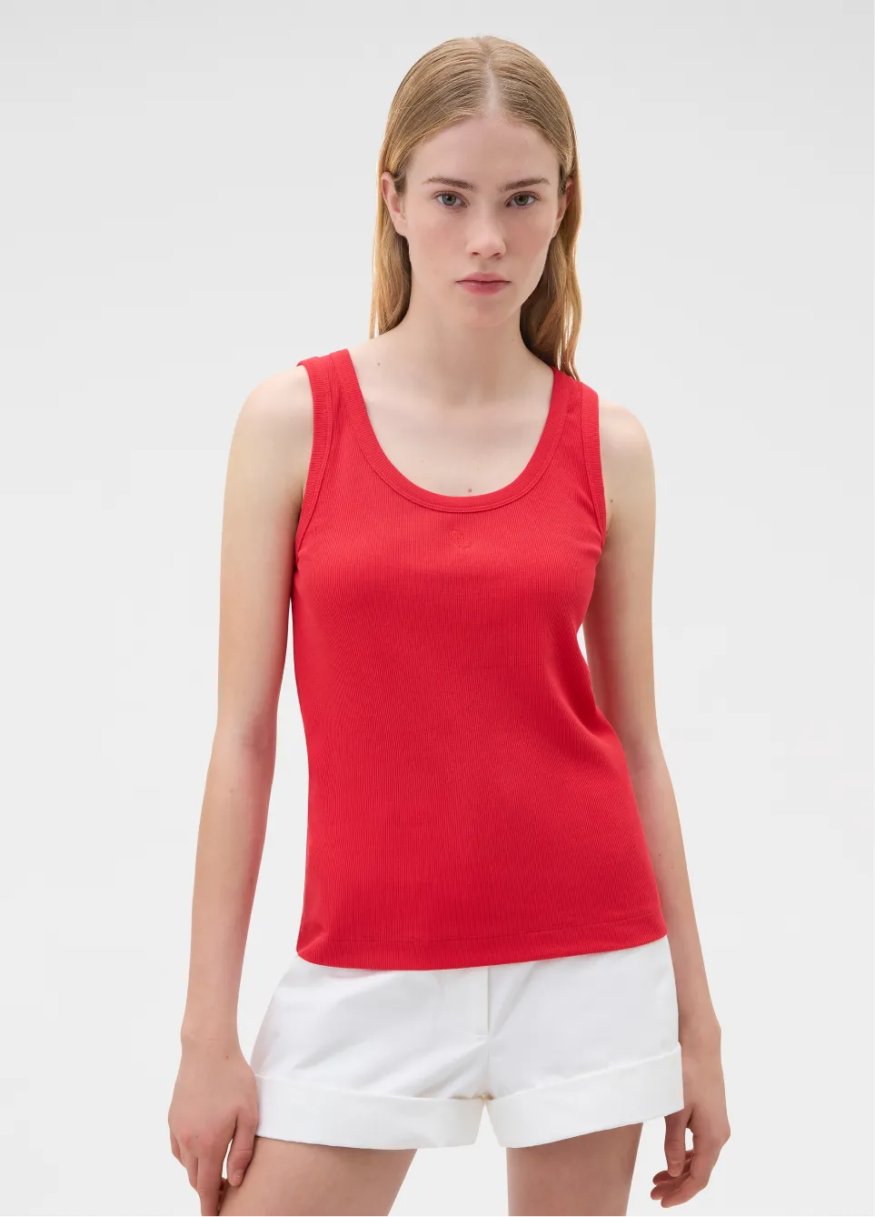 Woman in a red tank top and white shorts, looking confidently at the camera.