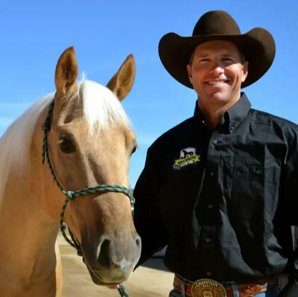 Brad Barkemeyer in a long sleeve black button up shire holding a beautiful fawn colored horse.