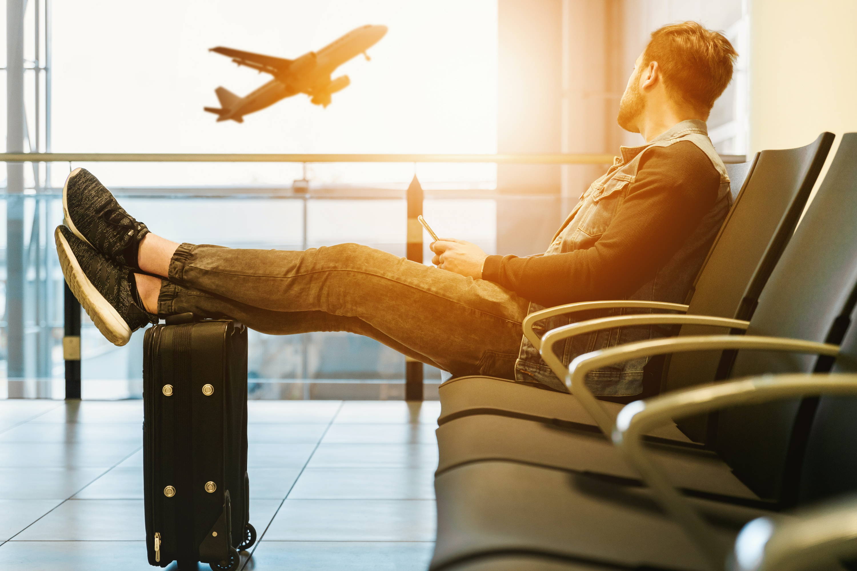 Hombre descansando en la sala del aeropuerto con los pies en alto viendo despegar los aviones