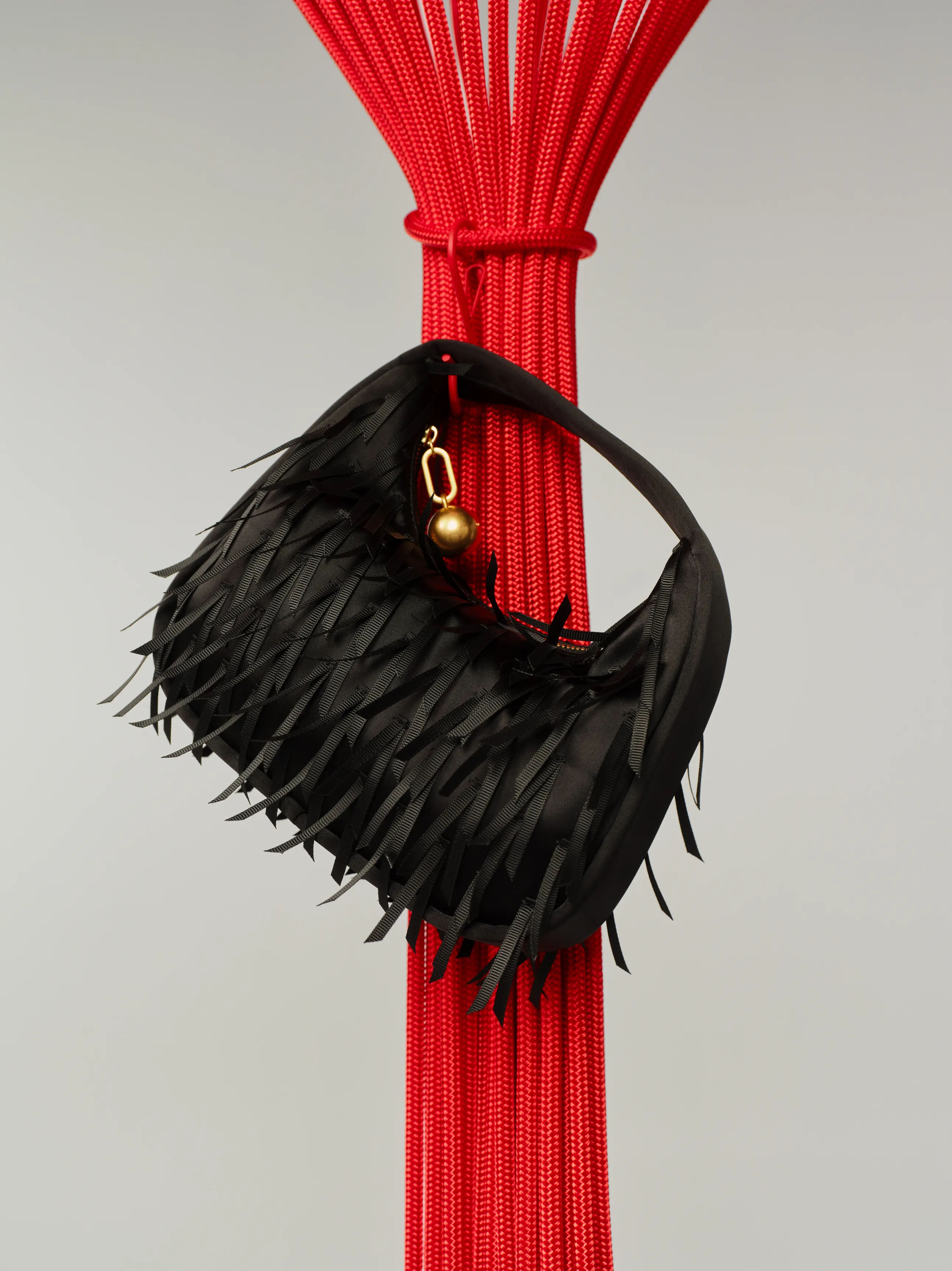 Black fringed handbag hanging from a red decorative pole.