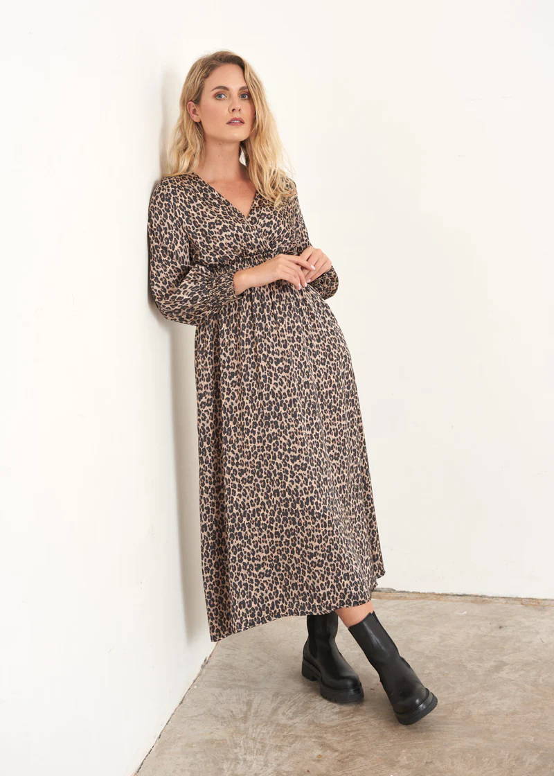 A model wearing a satin, midi length dress with long sleeves and a brown and black leopard print pattern and black leather chelsea boots