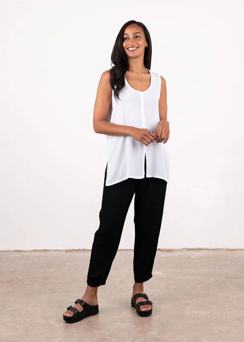 A model wearing a semi sheet, white cotton sleeveless top with split seam in the bottom middle hem, black trousers and black chunky platform slides