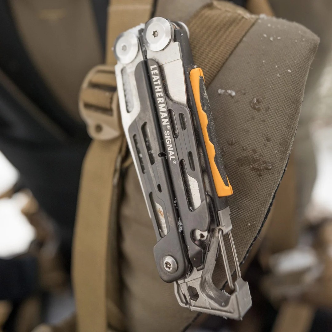 A multi-tool clipped to a backpack strap in a rugged outdoor setting.