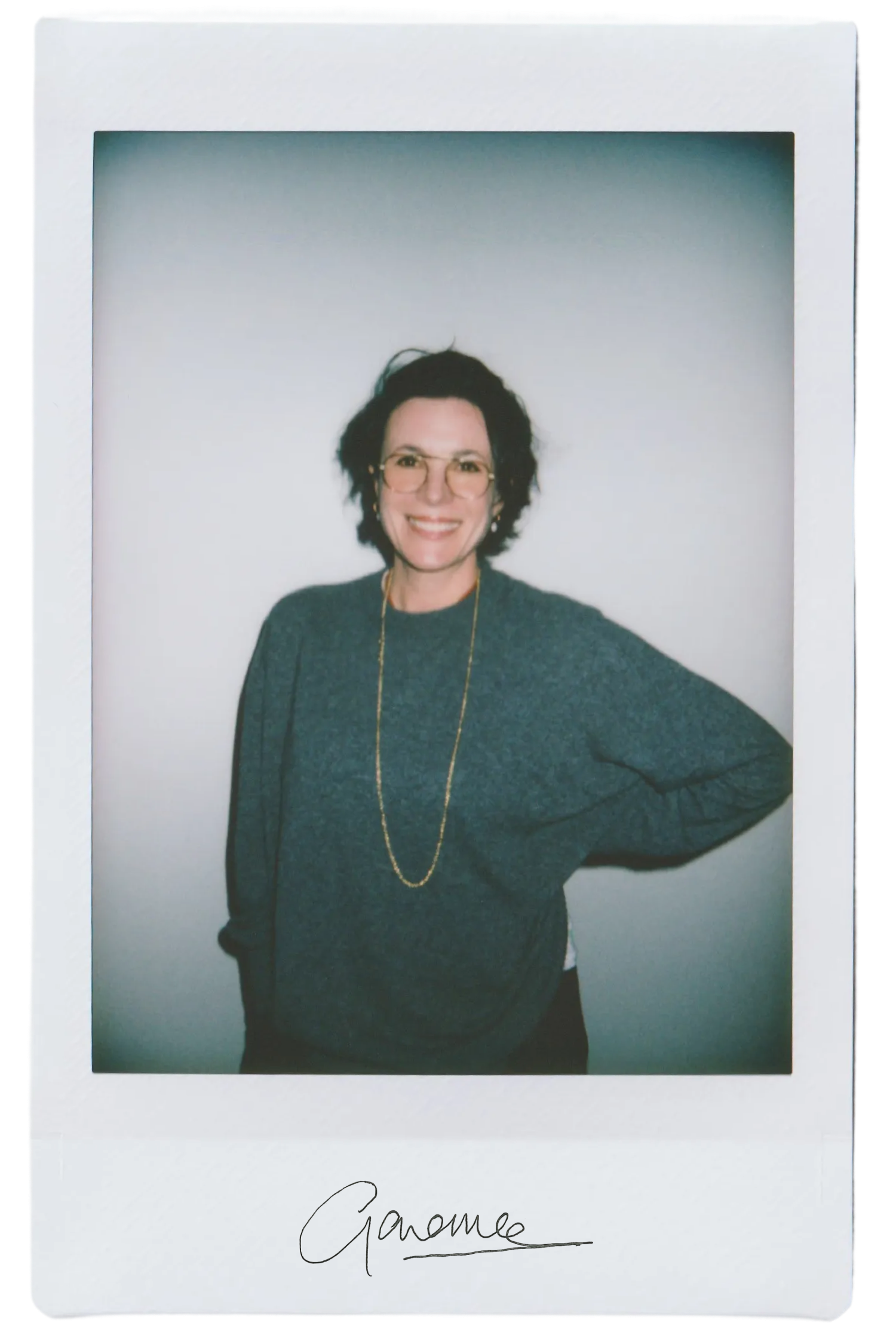 Smiling person in a gray sweater with glasses, standing against a plain background.