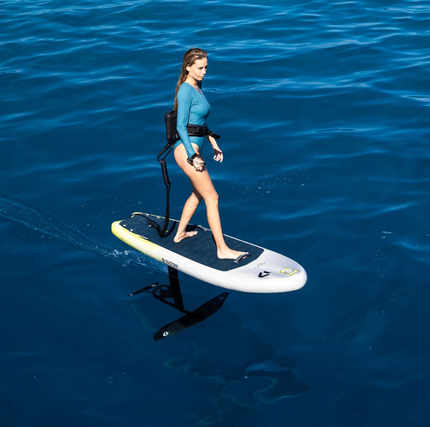 Person riding a e-foil surfboard over calm blue water.
