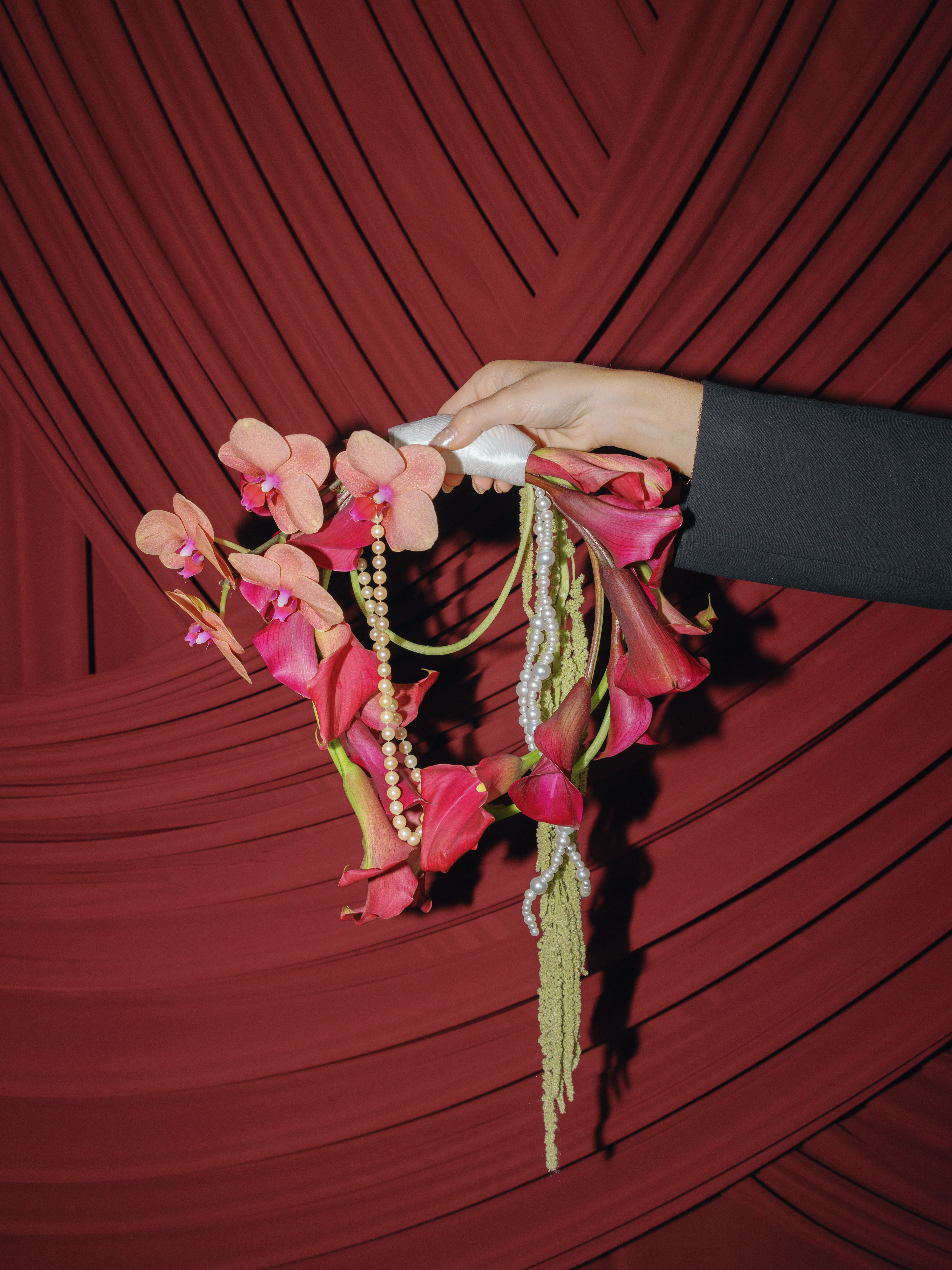 A hand holding a floral arrangement against a red draped background.